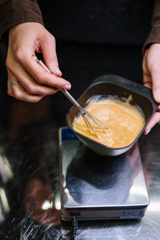 hair dresser mixing a container of bleach in a black dish with a wire wisk